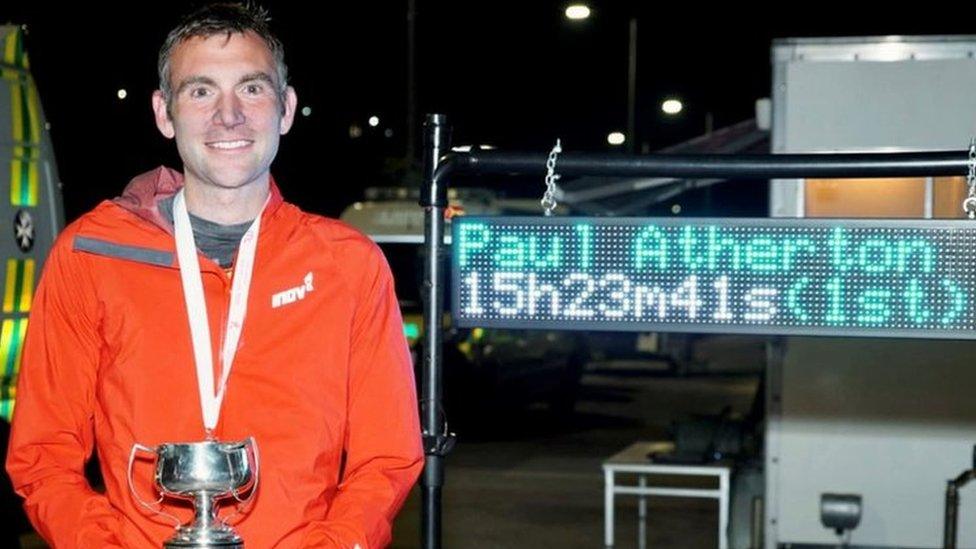 Paul Atherton holding the trophy with his finishing time on a board behind him