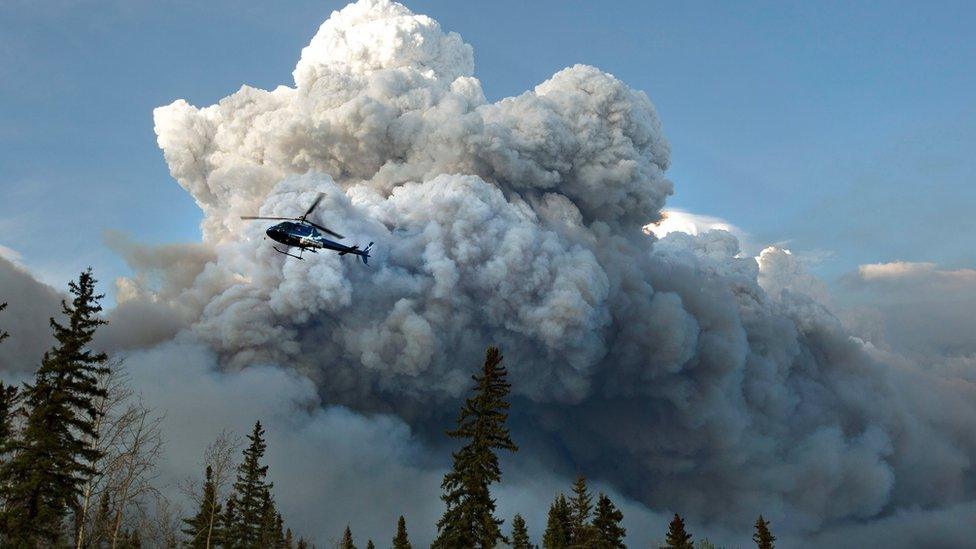 A chopper flies over smoke from wildfires in Alberta, Canada