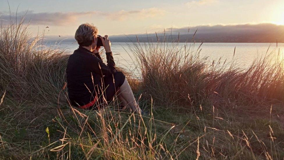 Noreen Mack sitting in the grass photographing the sunset.