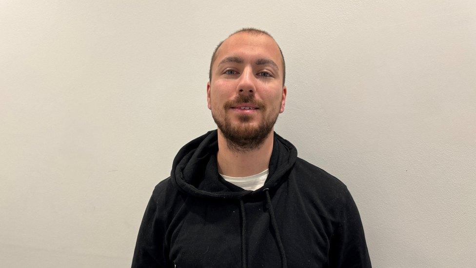 Man with very short dark hair and short beard wearing a black hoodie