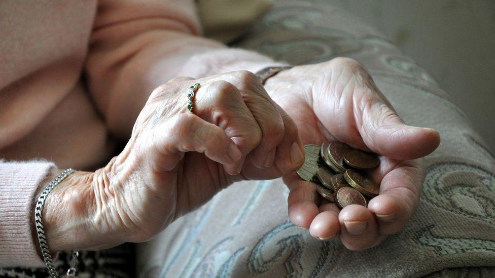 An elderly woman holds coins in her hands 