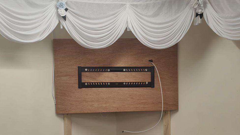 An empty TV wall bracket in a room where a large TV screen has clearly been taken and stolen. Above the TV wall bracket is some wedding decorations for an upcoming celebration booked at the Guisborough Town FC clubhouse.