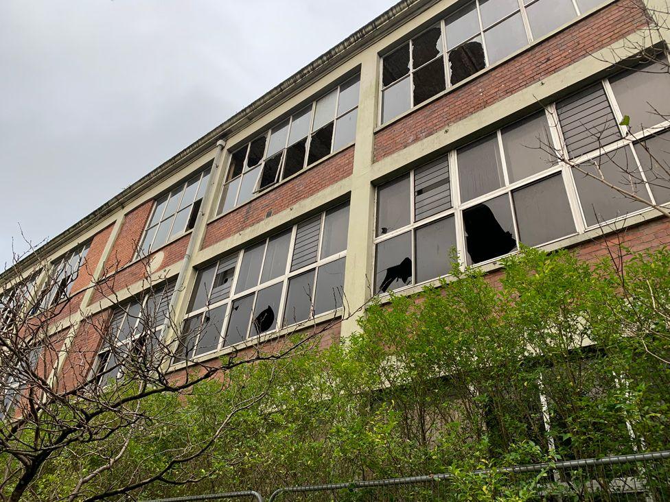 A row of factory windows viewed from the ground with many of them missing or broken