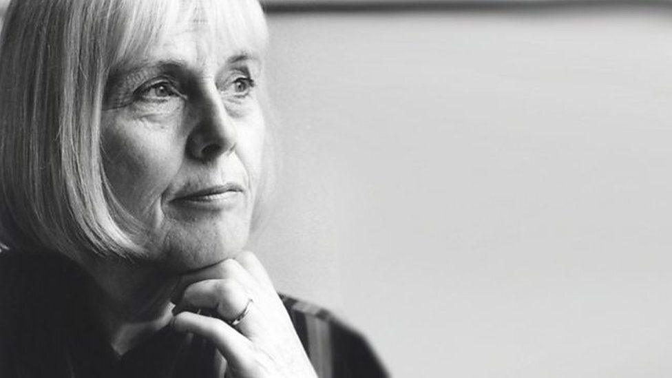 A black and white candid photo of a woman gazing at something away from the camera. There is a ring on her finger