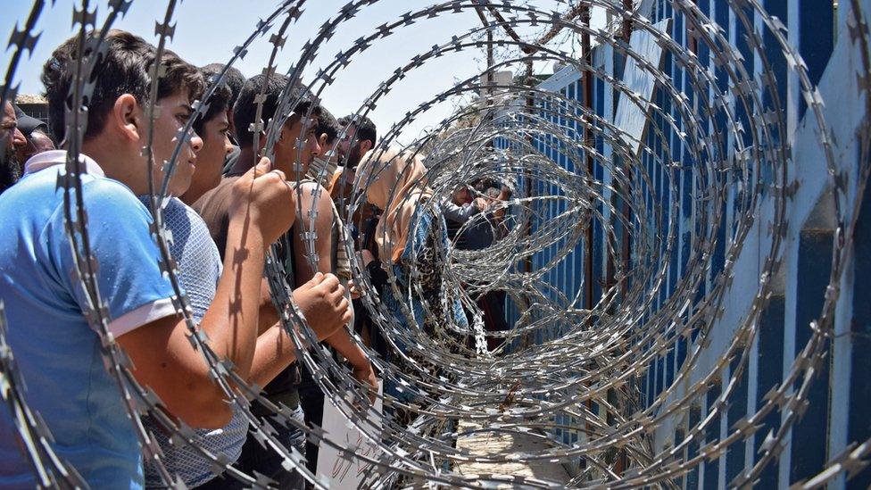 Youths from a camp for the displaced at in the Syrian village of al-Rafid hold the barbed-wire fence near a checkpoint along the border with the Israeli-occupied Golan Heights (4 July 2018)