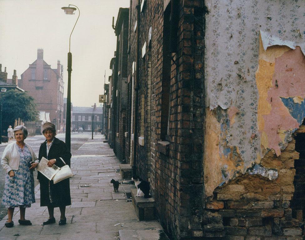 Two women stand in a run-down residential street