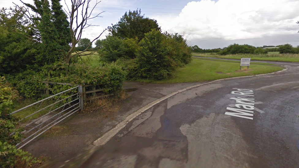 Mark Road in Highbridge, Somerset, with fencing and trees alongside the road