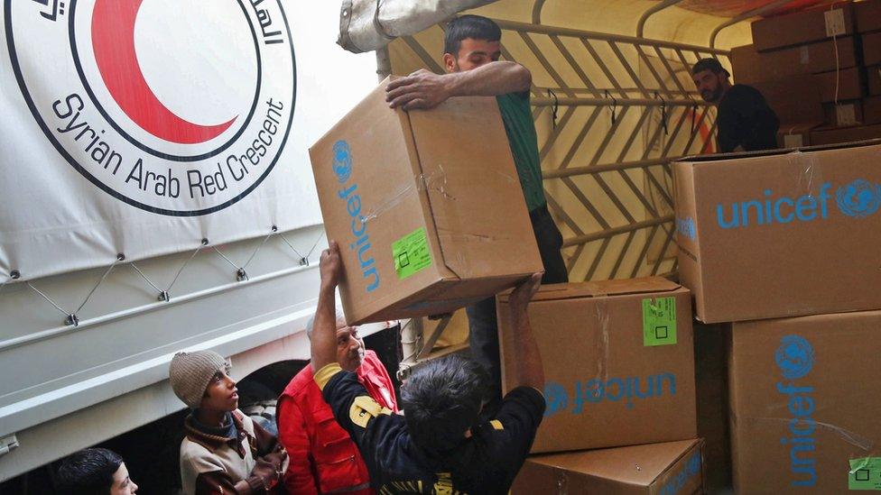 Syrian children watch as aid packages are unloaded in Nashabieh, in the Eastern Ghouta area outside Damascus (28 November 2017)