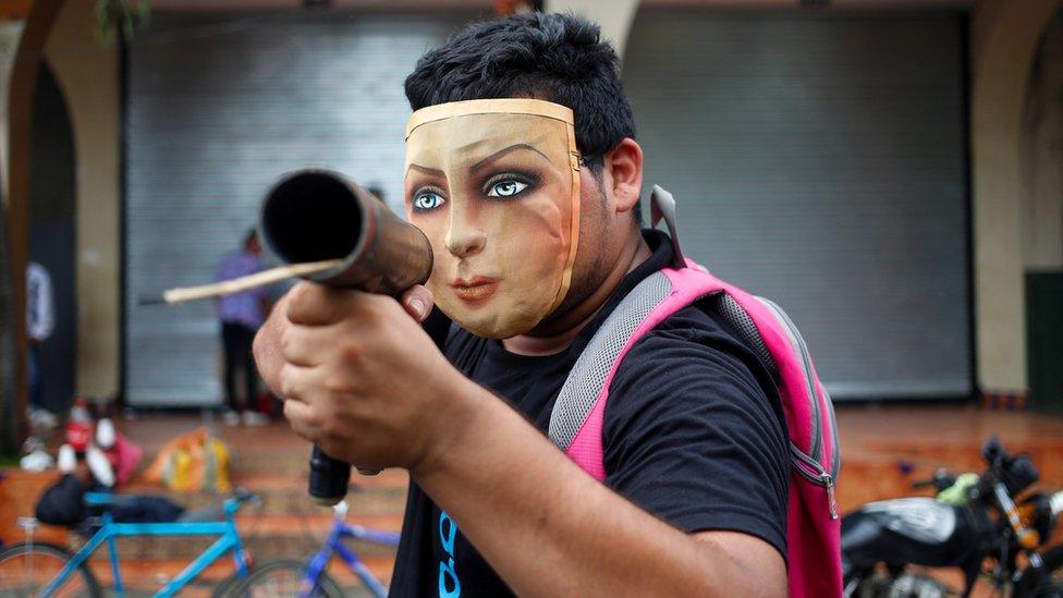 A demonstrator poses for a photo with his homemade mortar pointed directly at the camera, face covered by a cloth mask of a woman's face