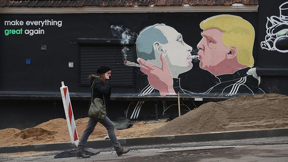 A woman walks past a mural of Donald Trump (R) blowing marijuana smoke into the mouth of Vladimir Putin in Vilnius, Lithuania