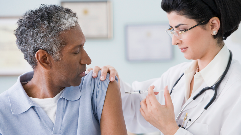 Flu jab being given to male patient in arm by female GP