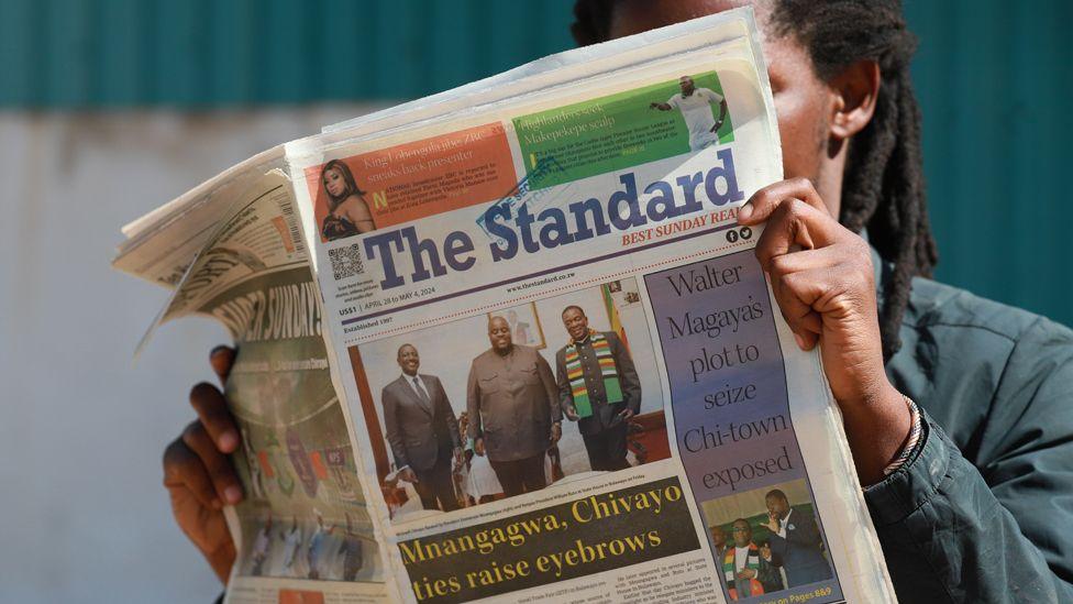 A man reading The Standard newspaper from early May with a photo of Wicknell Chivayo standing between Kenya's President William Ruto (L) and Zimbabwe's President Emmerson Mnangagwa (R)