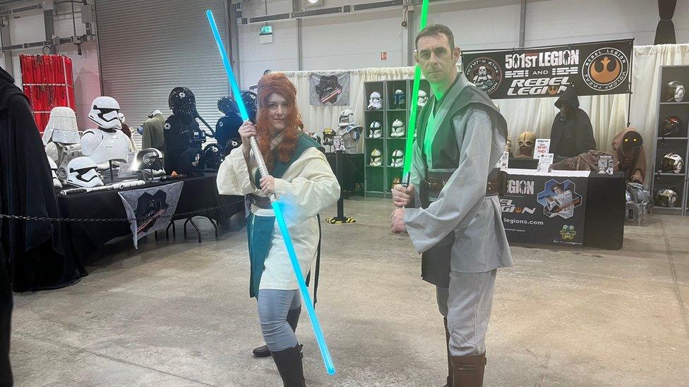 Two cosplayers stand with lightsabers