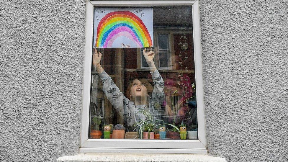 Child putting rainbow picture in window