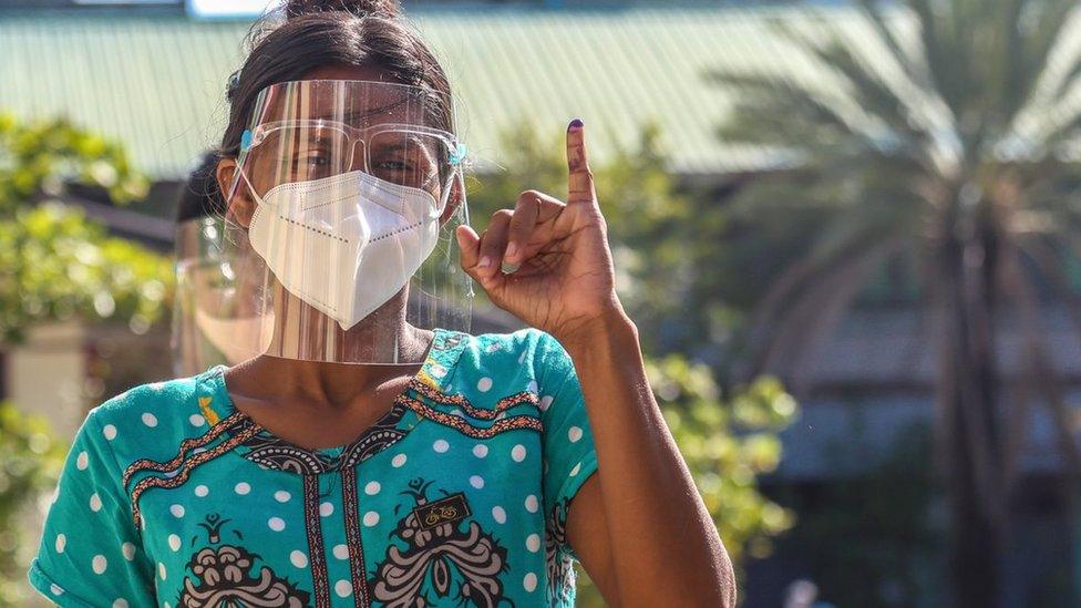 A woman is raising her inked finger in front of the polling station after she finished to vote in November 2020