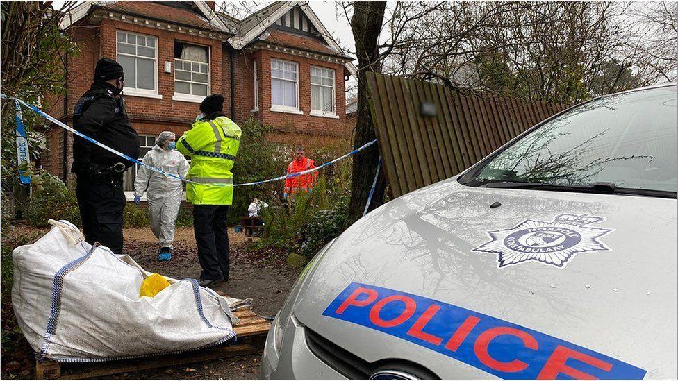 Fire-damaged house, police cordon, officers and police vehicle