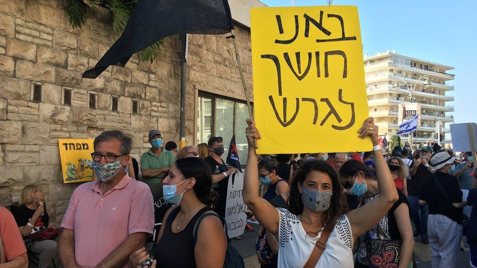 Adi Rosenthal holds a sign which reads: We come to banish the darkness