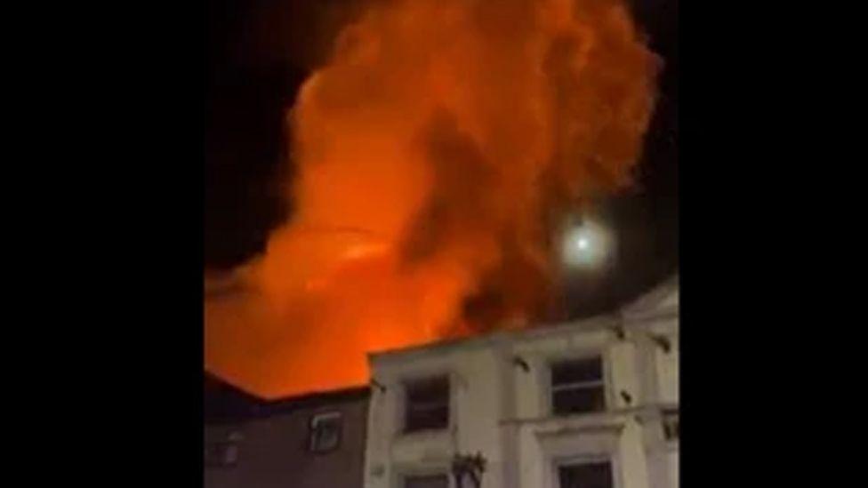 Orange flames leap into the sky from a derelict building behind shops in Church Street, Preston