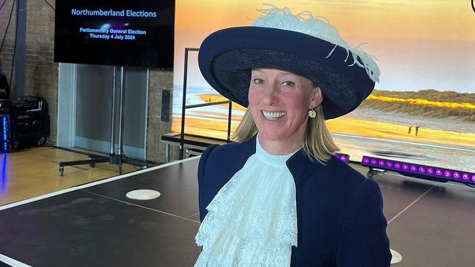 Lucia Bridgeman smiling at the camera, wearing her navy blue hat with white feathers