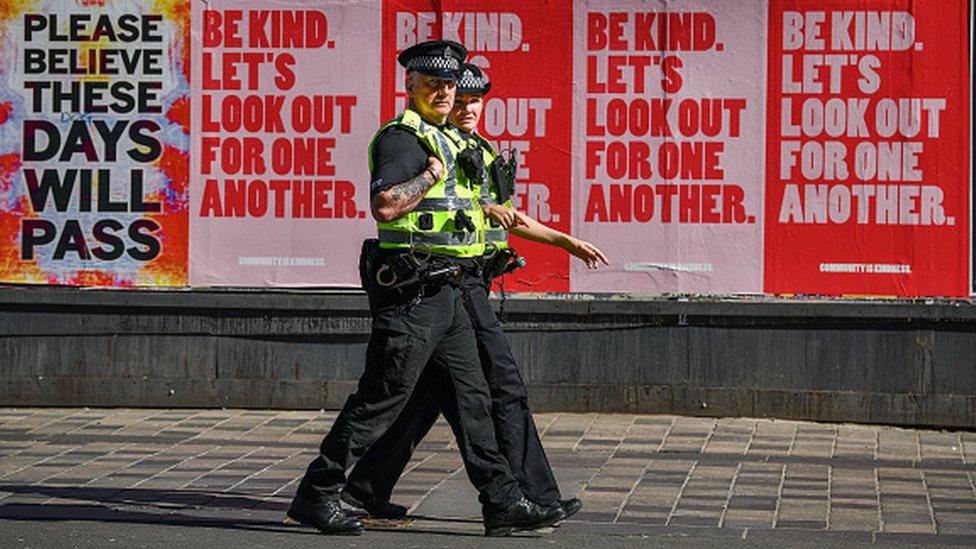 A pair of police officers walking with pink and red advert billboards behind them