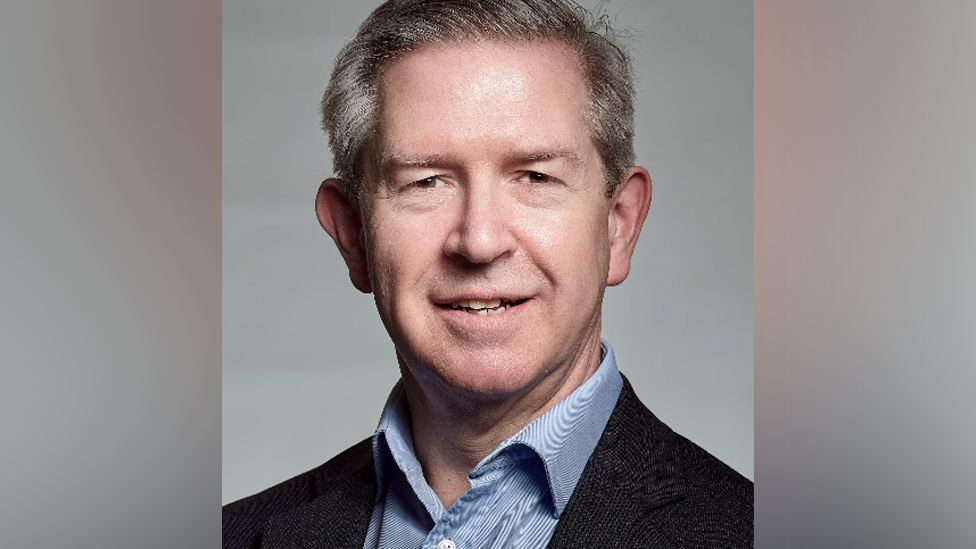 Head and shoulders image of Duncan Eldridge, wearing a blue striped, open-neck shirt under a dark suit jacket