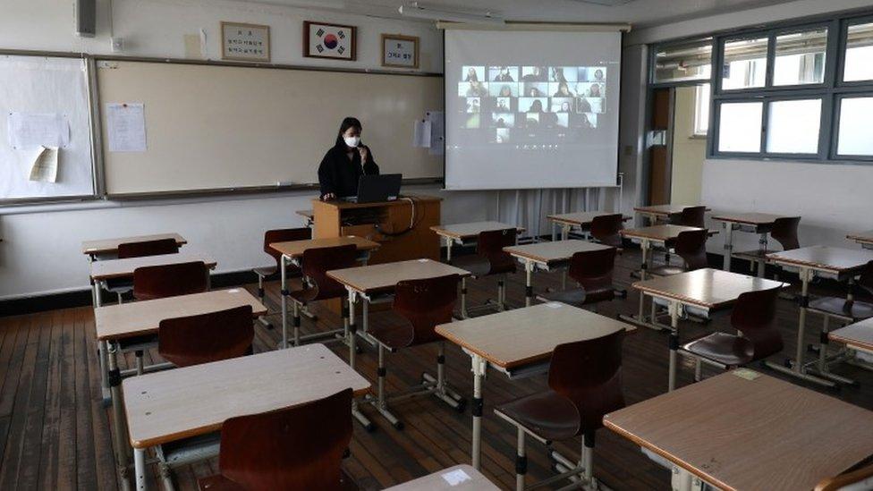 Teacher in empty classroom giving online class to pupils via video link