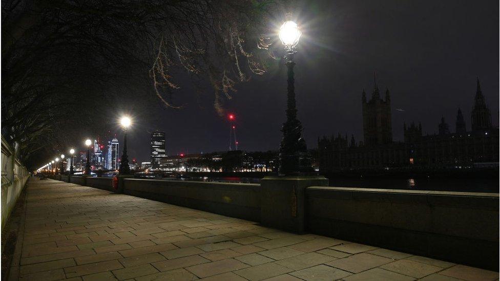 A picture taken on March 27, 2021 in central London shows the Palace of Westminster (R), home to the Houses of Parliament which include the House of Lords and House of Commons, submerged into darkness