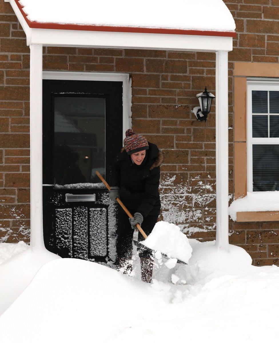 A woman clears snow from a doorway