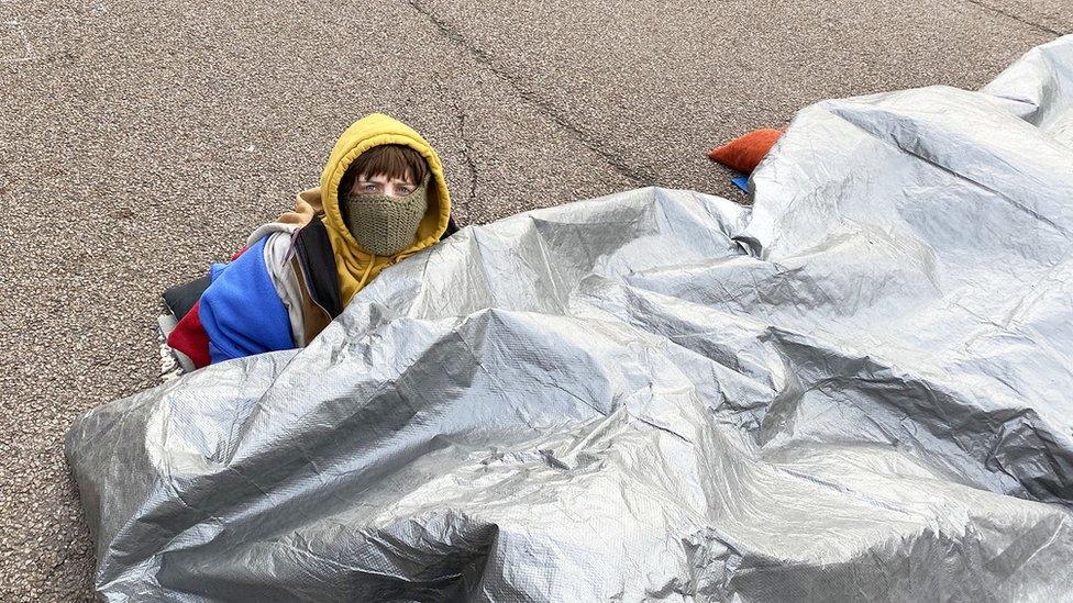 A protesters beneath a silver-coloured tarpaulin outside the Lockheed Martin site