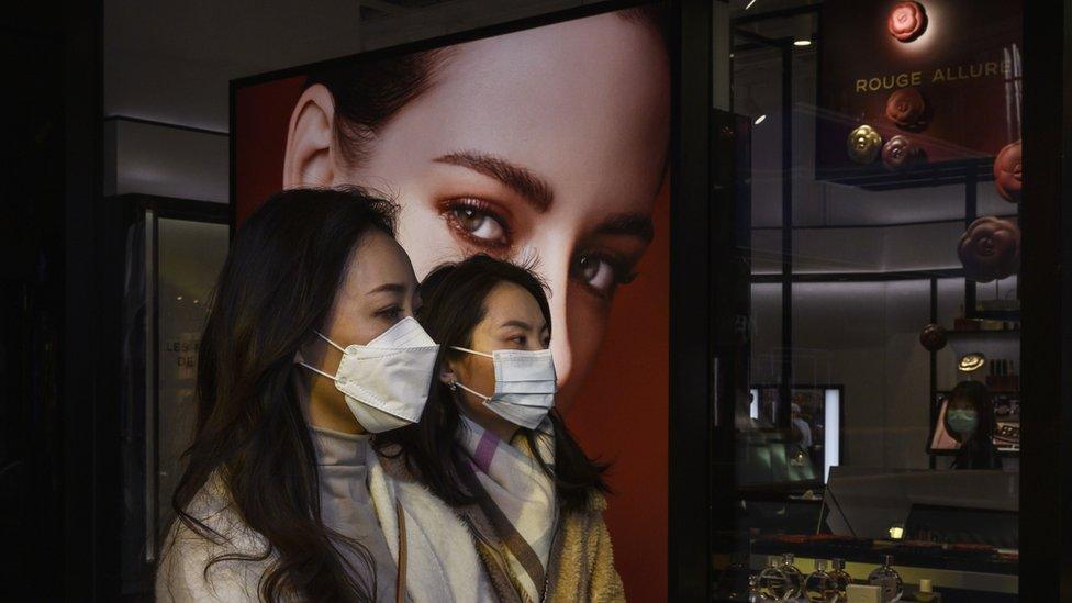 Women wearing masks in a Chinese shopping centre walk past a billboard of a white woman