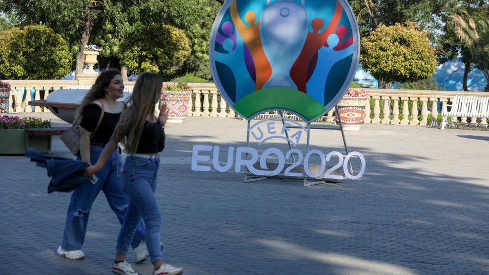 Two woman walk past a sign promoting Euro 2020 in Baku