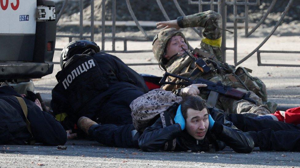 People take cover as an air-raid siren sounds near an apartment building damaged by shelling in Kyiv on Saturday