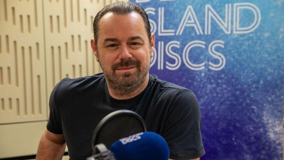 Danny Dyer sits smiling in front of a Desert Island Discs backdrop.