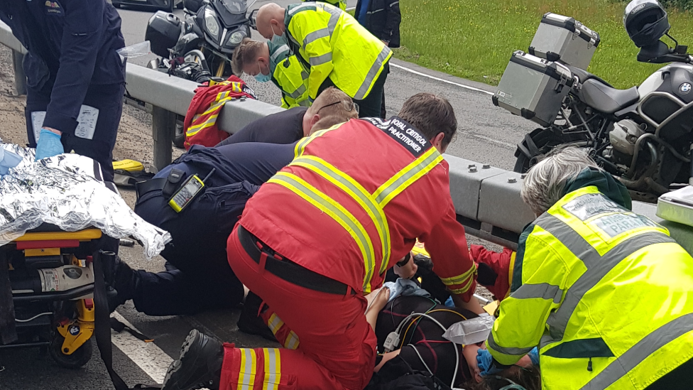 Paramedics crouch around a patient on a roadside