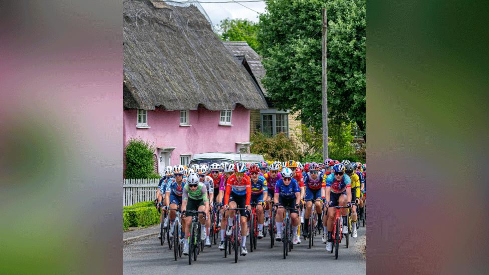 Ride London cyclists riding along a road, with the backdrop of a pink thatched cottage