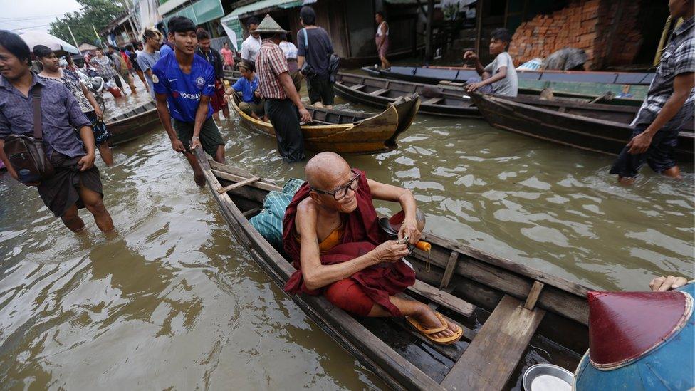 Buddhist monk sits on the boat as people use boat to pass through flooded road