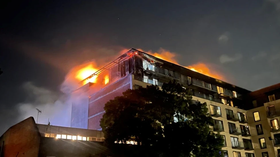 A picture of the fire in Mosaic Apartments in Slough, with clear fire ablaze at the top of the building, with smoke and fire spreading along the top floor of it.