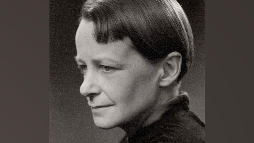 A black and white photo of Nan Youngman. She is in profile and slightly turning to the right so both her eyes can be seen. She has a relaxed face and short sleek hair, tucked behind her ear. She is wearing a dark top. 