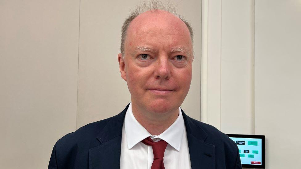 Chris Whitty wearing a suit and red tie.