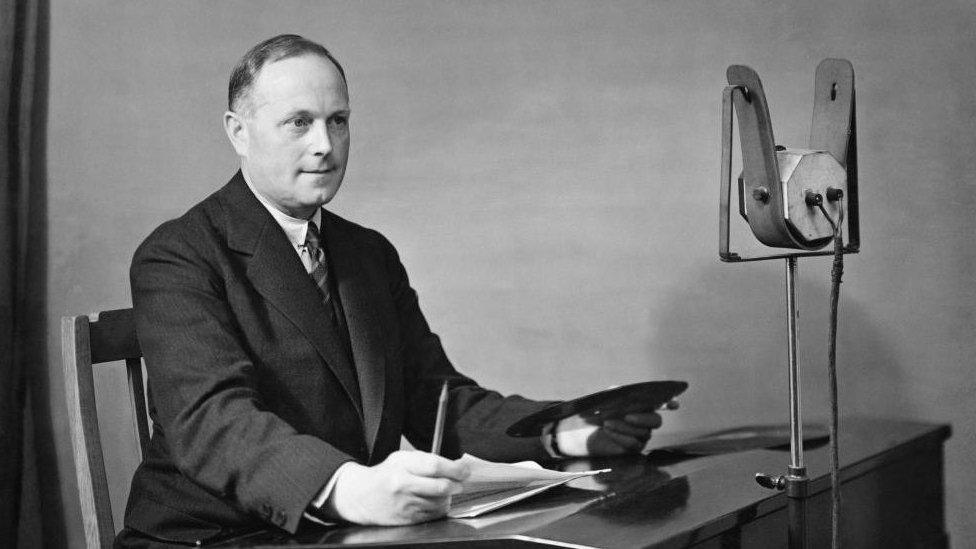 Arthur Burrows sits at a desk in front of a microphone