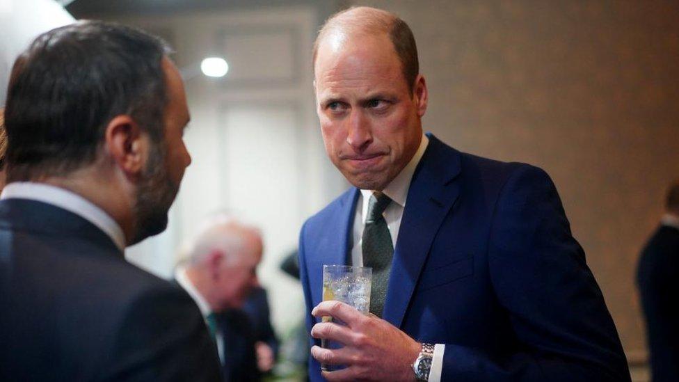 Prince William is in conversation, holding a beverage