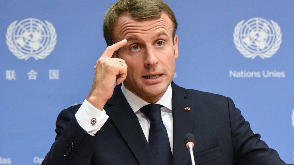 French President Emmanuel Macron pointing to his head.