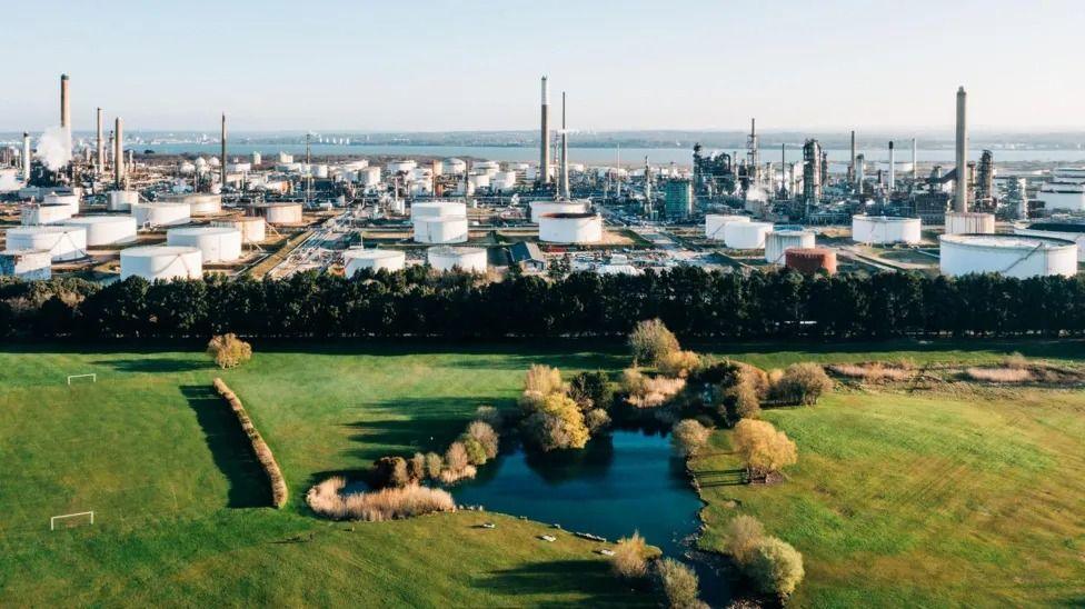 Fawley Manufacturing Complex is a large sprawling series of thin white towers and short round disc-shaped structures, in front of a large body of water