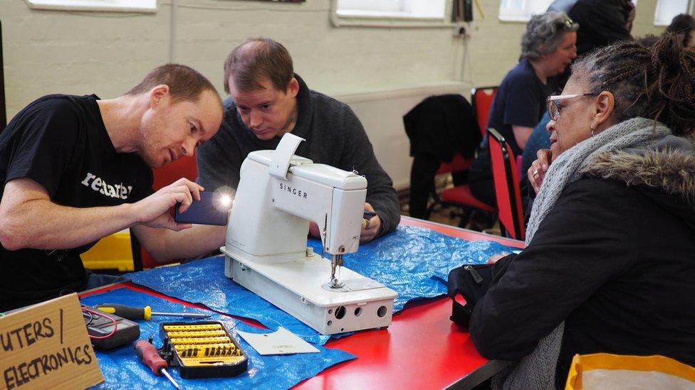 Two men with tools take a look at a broken sewing machine.