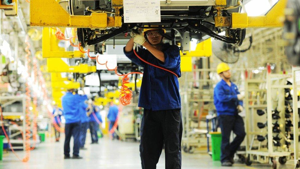 Workers install car parts at their assembly line in a factory in Qingdao, China