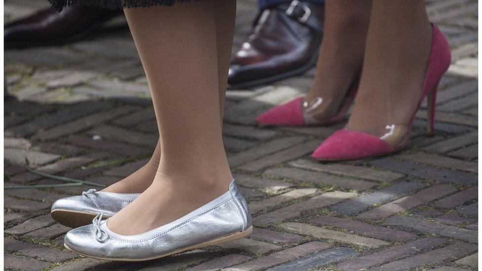 Man in flat smart shoes standing next to a woman in high heels and a woman in flat shoes