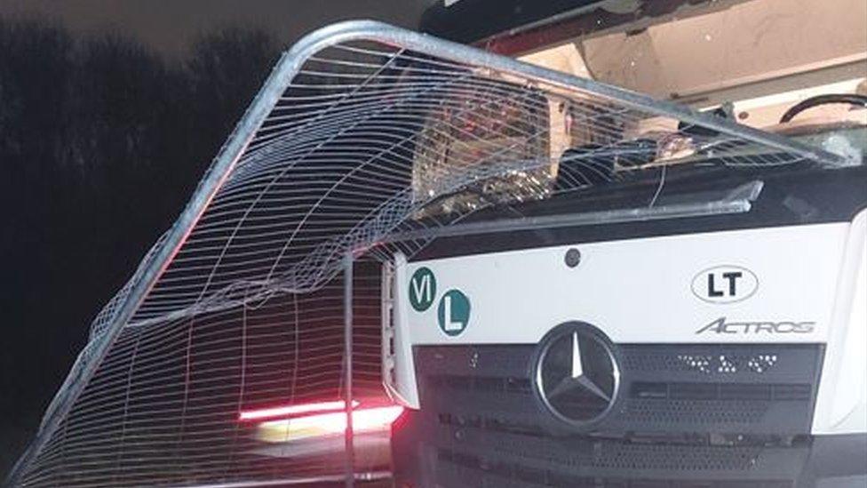 White Mercedes-Benz lorry with a metal fence panel embedded in the windscreen