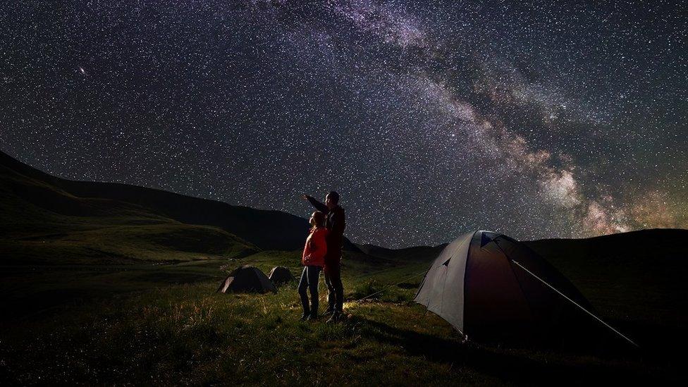 A father and a child, camping, admiring the starry night sky