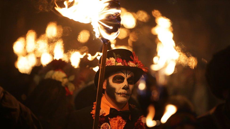 Man with skull face paint carrying a torch