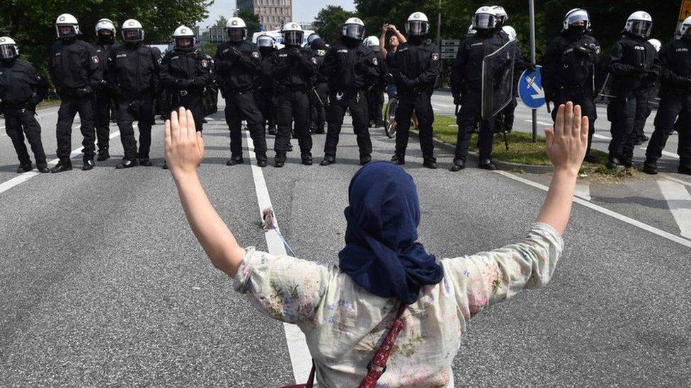 A demonstrator holds her hands up as she faces policemen during a protest on July 7, 2017 in Hamburg, northern Germany, where leaders of the world"s top economies gather for a G20 summit